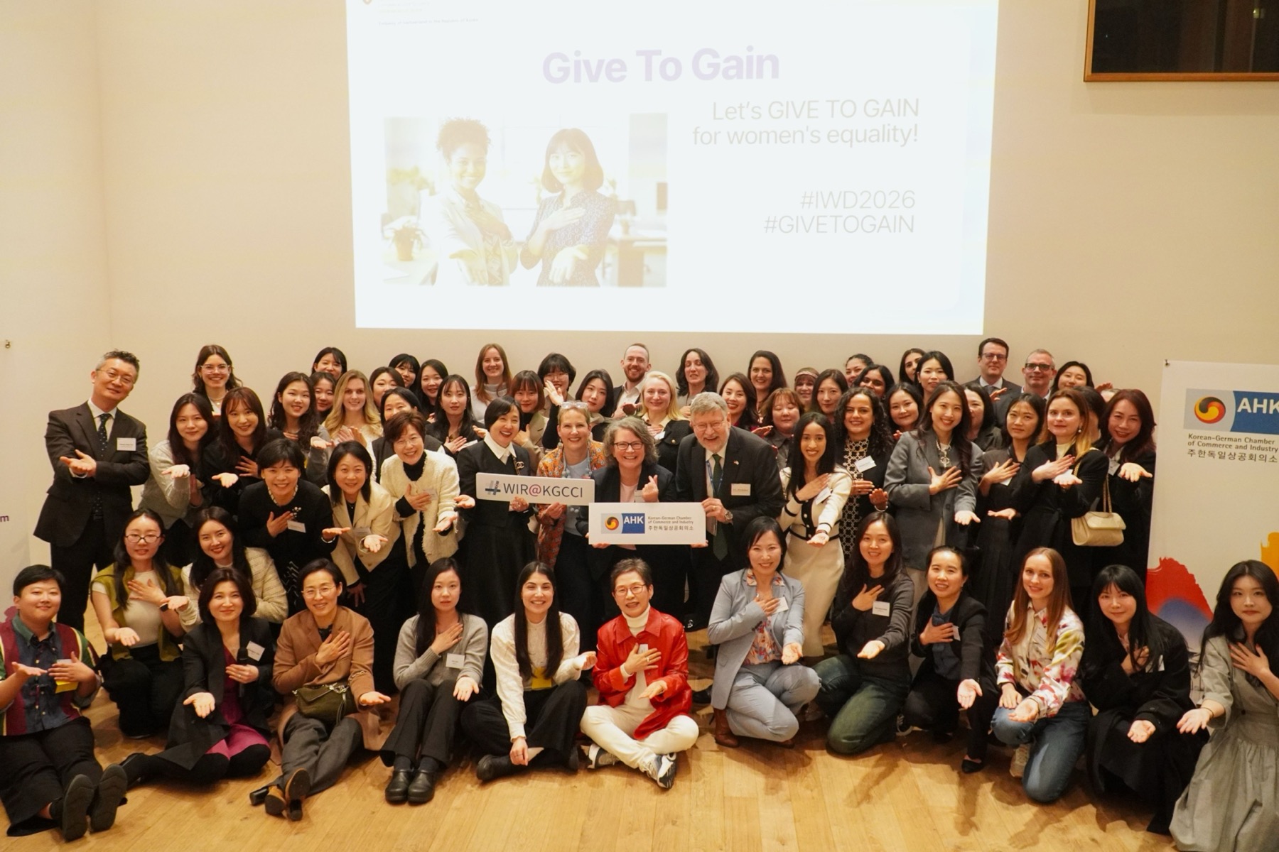 A full room of the Women In koRea network at an International Women’s Day event, under a screen reading Give To Gain